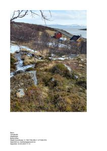 Fotografi av et landskap med to små hytter (en rød og en gul) i bakgrunnen, sett fra et høyere punkt. Bildet viser terreng, vegetasjon, en vei og vann i fjernheten.