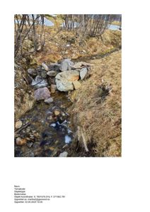 Fotografi av en bekke eller liten elv med steiner og snørest i et naturlig landskap.