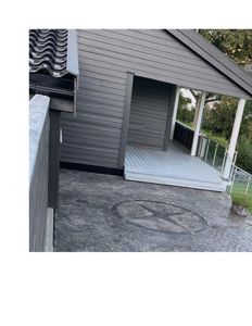 Fotografi av en gråbeiglet bygning med en utvendig terrasse, en betongplassering med et mønster i midten, og en del av en gjerdevegg.