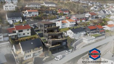 Luftfoto av et boligområde med en fremtredende, mørk, moderne bygning i midten. Bildet viser eksisterende eller planlagt bebyggelse i et nabolag.