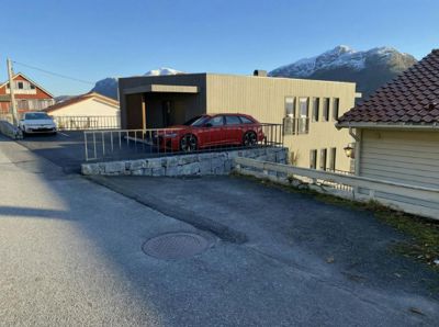 Fotografi av en moderne bygning med en rød bil parkert foran, sett fra gaten med fjell i bakgrunnen.