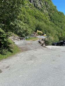 Fotografi av en byggeplass eller tomt med grusvei, parkeringsplass, grøfting og en gulelastbil i bakgrunnen.