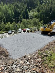Fotografi av en byggeplass med en nygravet grusflate, en gullgraver og en vei i bakgrunn.