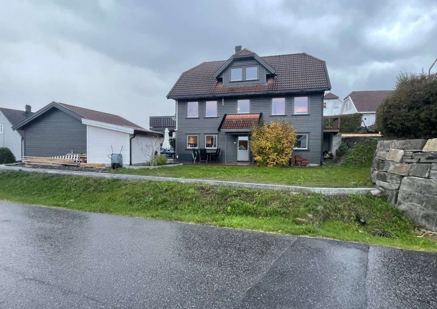 Fotografi av en grå villa med garasje og hage sett fra veien.