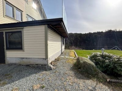 Fotografi av en bygning sett fra siden, som viser fasade, vinduer, tak og omgivende hage.