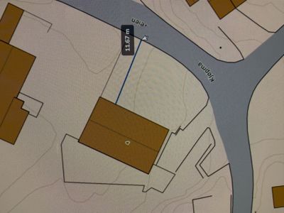 Et digitalt kart eller situasjonsplan som viser eiendomsgrenser, bygninger (brune felter), veier (grå felt) og en målestrekning på 11,67 m.