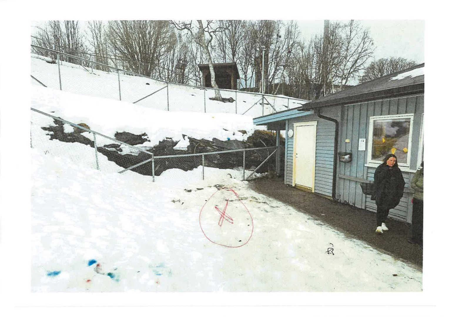 Fotografi av en eksisterende bygning (hus) sett fra siden, med snø på bakken og en person som står på verandaen.