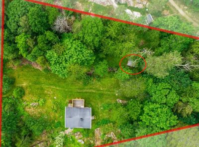 Luftfoto av en tomt med en hytte og skog. Bildet viser tomtens grenser markert med røde linjer og en sirkel rundt en annen bygning.