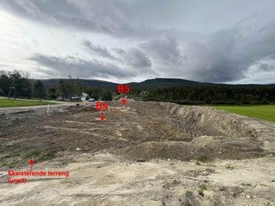 Fotografi av et utgravet byggeområde med markerte punkter (B4, B5) og en tekstmarkering for eksisterende terreng.