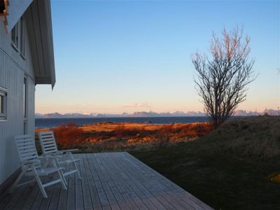 Fotografi av en hytte med utsikt over havet og fjell i bakgrunnen.