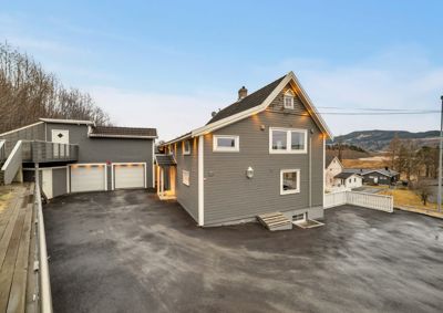 Fotografi av en moderne, grå ferdigstilt bolig med garasje og stor betongplass foran.