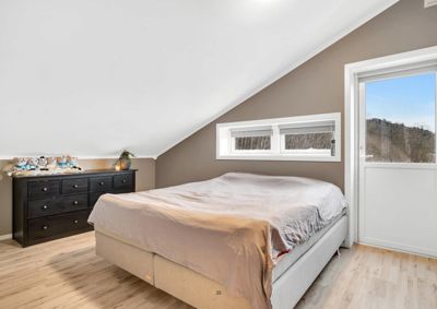 Fotografi av et innredet soverom med skrå tak, en seng, et skap og et vindu.