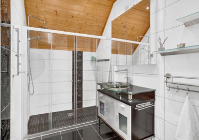 Fotografi av et moderne bad med dusj, vask og trepanel tak.