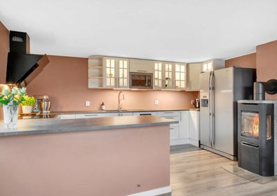 Fotografi av en moderne kjøkkeninnredning med øy, kjøleskap og peis.