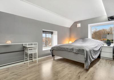 Fotografi av et innredet soverom med seng, skrivebord og vinduer.