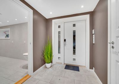 Fotografi av en inngangsparti i en bolig, med en hvit hoveddør, en plante og en del av et bad i bakgrunnen.