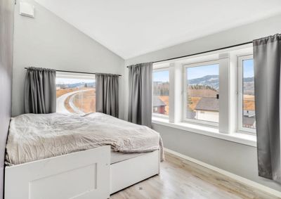 Fotografi av et soverom med en seng, vinduer og utsikt over landskapet.