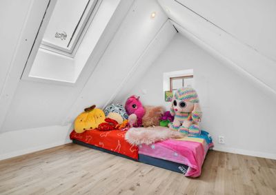 Fotografi av et innredet soverom i et skrått takrom med leketøy på sengen.