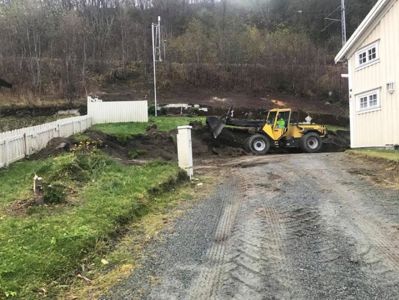 Fotografi av en byggeplass med en gaffeltruck som graver ved siden av en eksisterende bygning.