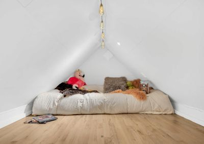 Fotografi av et innredet soverom i et skrått takrom med en madrass, leketøy og dekorasjoner.