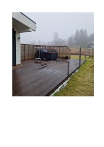 Fotografi av en terrasse med tredekk, hot tub og hekk sett fra bakkenivå.