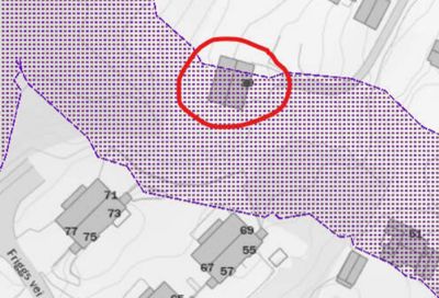 Kartutsnitt som viser et område med tomtegrenser (lilla prikket mønster) og flere bygninger med nummerering. En bygning er markert med en rød sirkel.