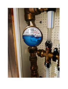 Fotografi av en gassmåler og tilhørende rørleggerutstyr (ventiler, kobber- og plastrør) montert på en vegg.