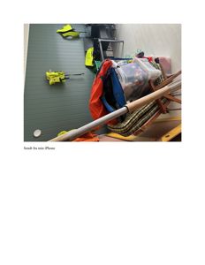 Fotografi av et rom med grønn panelvegg, hvor det henger gule verneutstyrer og ligger en stor pose med utstyr på gulvet.