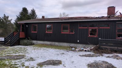 Fotografi av en svart hytte med røde vindusrammer, sett fra siden.