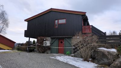 Fotografi av en mørk trehus med en grønn garasjeport og en rød dør, sett fra bakkenivå.