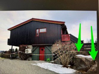 Fotografi av en mørk trehytte med en rød dør og et vindu, sett fra bakkenivå.