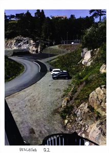 Fotografi av en vei som svinger inn mot en bygning i en kupert, bergig landskap.