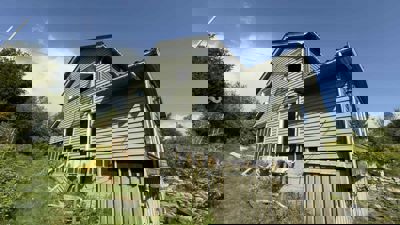 Fotografi av en grå hytte under renovering eller utvidelse, sett fra en skrå vinkel.