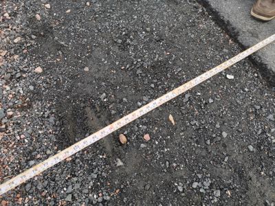 Fotografi av en målebånd som ligger på grus, sannsynligvis for å måle en avstand eller dimensjon på en byggeplass.