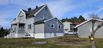 Fotografi av en grå ferdigstilt villa med hvit grunnmur og balkong, sett fra bakgårdssiden.