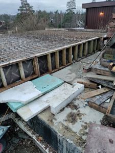 Fotografi av en byggeplass som viser en ferdigstilt betongplate med armering og en delvis ferdigstilt betongvegg i bakgrunnen.