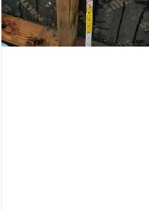 Fotografi av en byggeprosess eller konstruksjon, der det vises et målebånd som brukes til å måle en vertikal trekonstruksjon.