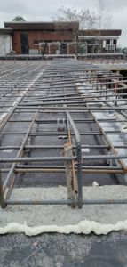 Fotografi av en byggeplass som viser etablering av armeringsnett for betonggulv eller -plate, med en ferdig fasade i bakgrunnen.