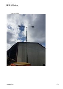 Fotografi av en høy lysmast foran en industribygning.