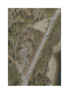 Flyfoto eller satellittbilde av et område med en vei (merket 450), skog, og vannkant.