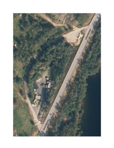 Flyfoto eller satellittbilde av et område med vei, skog og vann.