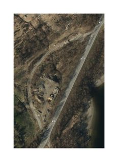 Flyfoto eller satellittbilde av et område med en vei, skog og en liten bygning.