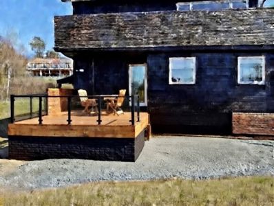 Fotografi av en mørk, toetasjes bygning med en uteplass foran. Bildet viser fasaden, vinduer, tak og omgivelsene.