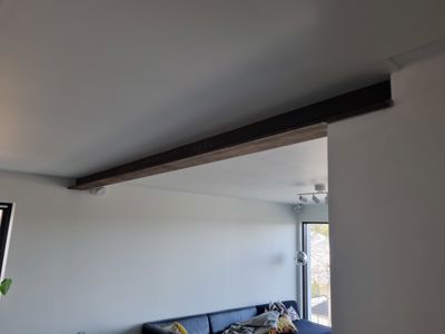 Fotografi av et interiør med en mørk bjelke i taket og en sofa i bakgrunnen.