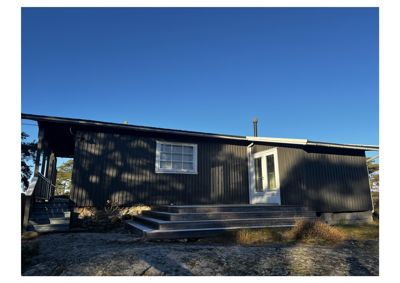 Fotografi av en mørk, langhusformet bygning sett fra siden. Bildet viser fasaden med vinduer, dører, trapper og en del av omgivelsene.