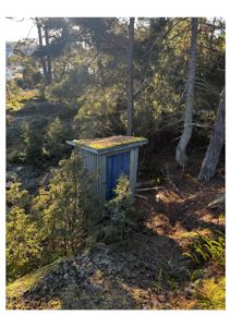 Fotografi av en liten, grå hytte med blå dør og mosede tak, plassert i et skogsterrang.