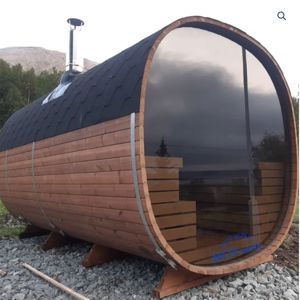 Fotografi av en ferdigstilt, sylindrisk tre-sauna med glassfront og skorstein.