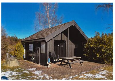 Fotografi av en mørk hytte eller utedo med utemøbler og snø på bakken.