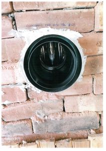 Fotografi av en rund ventilasjonssluks i en murvegg under bygging eller renovering.