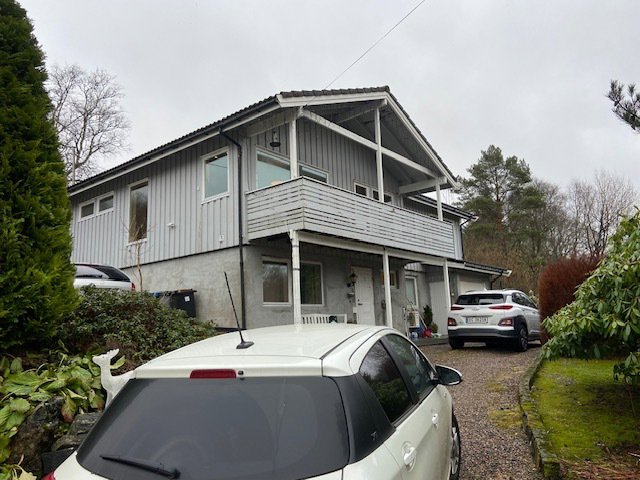 Fotografi av en eksisterende toetasjes bolig sett fra siden, med bil i forgrunnen.